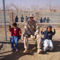 Josh Aldred sitting on swing next to two children in Afghanistan