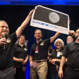 Alan Stern holds pluto poster above his head in crowd