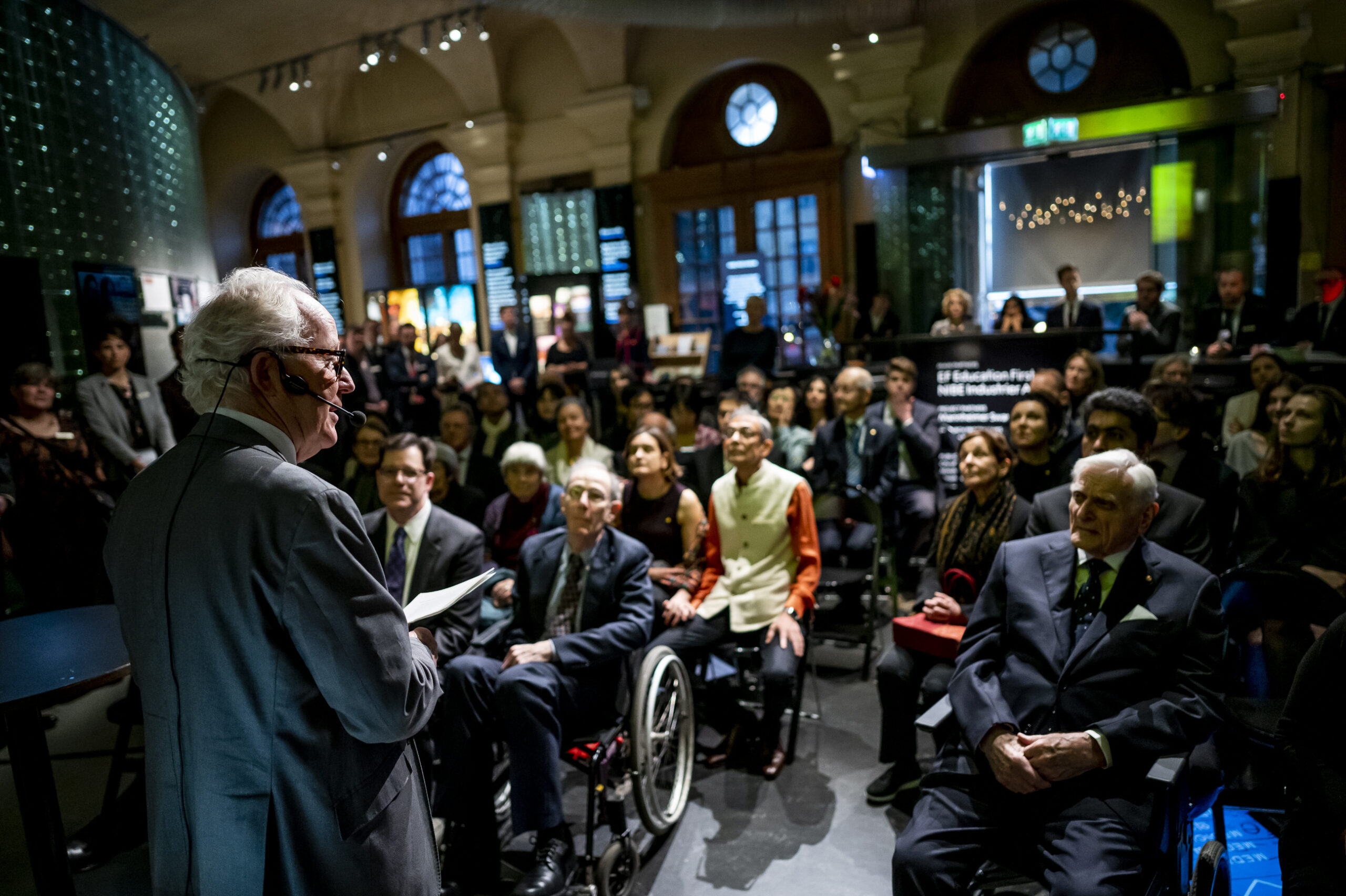 2019 nobel laureates listening to a speaker at the nobel museum