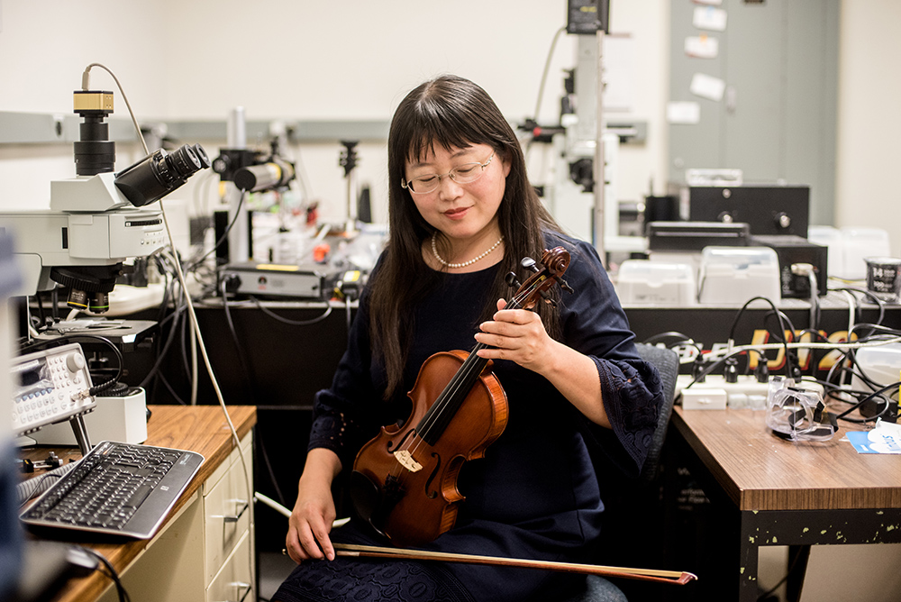 Professor Donglei (Emma) Fan holds violin and bow while sitting in lab