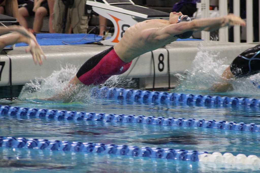 Swimmer dives back into pool lane from wall, to other swimmers on either side