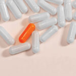 Several white pills on a table with one orange pill