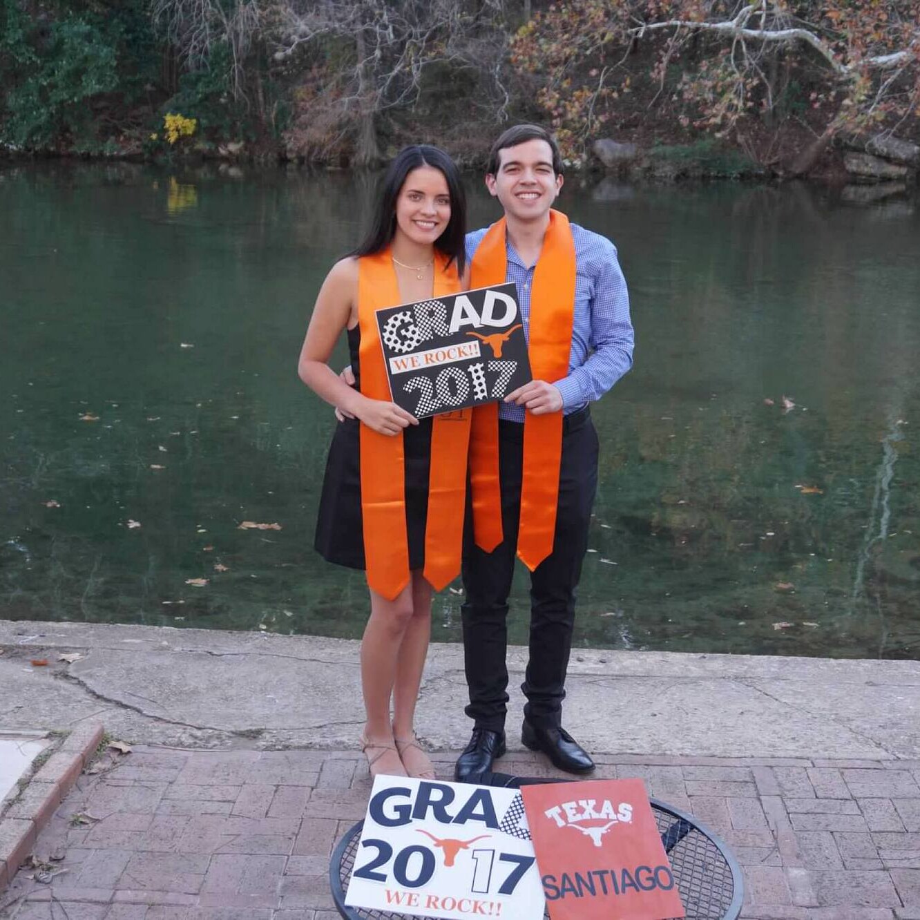 Texas Engineers Laura Rivera and Santiago Echeverri holding graduation sign by a lake