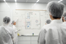 Texas Engineering students in lab gear looking at presentation at white board