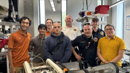Texas Engineers, including Siddharth Thakur, smiling with firefighters in lab space with firebot prototype