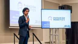 Texas Engineer Siddharth Thakur holding microphone in front of slides as he presents at New Ventures competition