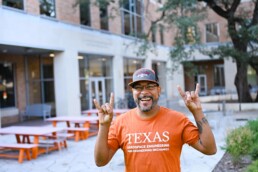 Guillermo Nieves smiling and doing hook 'em horns hand sign outside