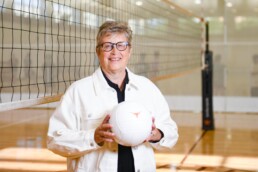 Michele Meyer holding volleyball in front of net at gym