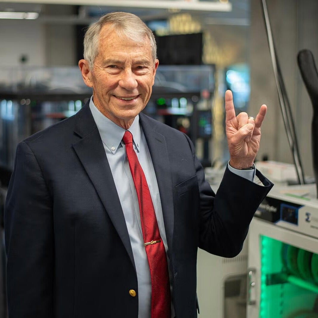 Texas Engineer Chuck Corley doing hook 'em hand sign in lab next to 3D printed hand