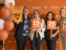 Michele Myer holding up hook 'em horns foam hand at Staff Appreciation event with colleagues.