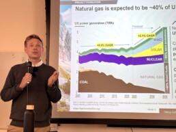 Speaker holding microphone in front of Open Mind meeting presentation on natural gas