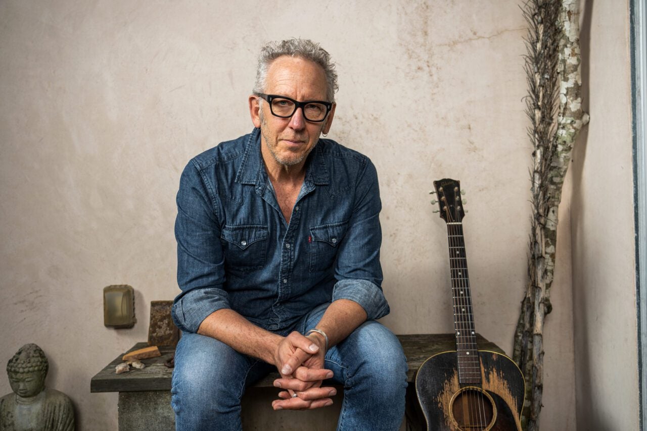 Darden Smith sitting with guitar on bench outside